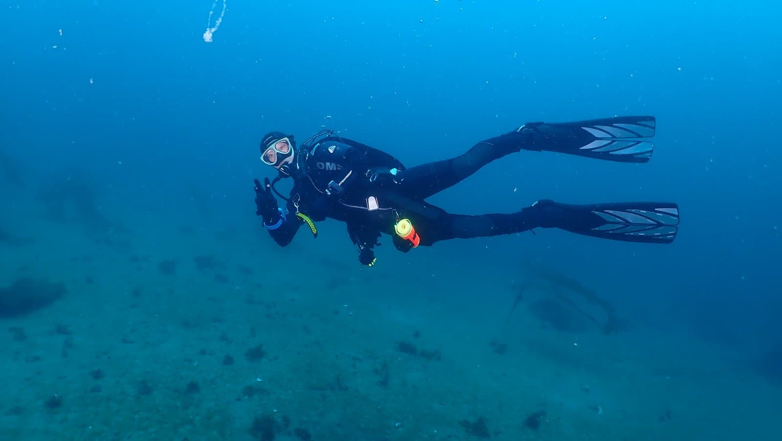 Hovering over the sandy bottom flashing a peace sign and holding a dive light