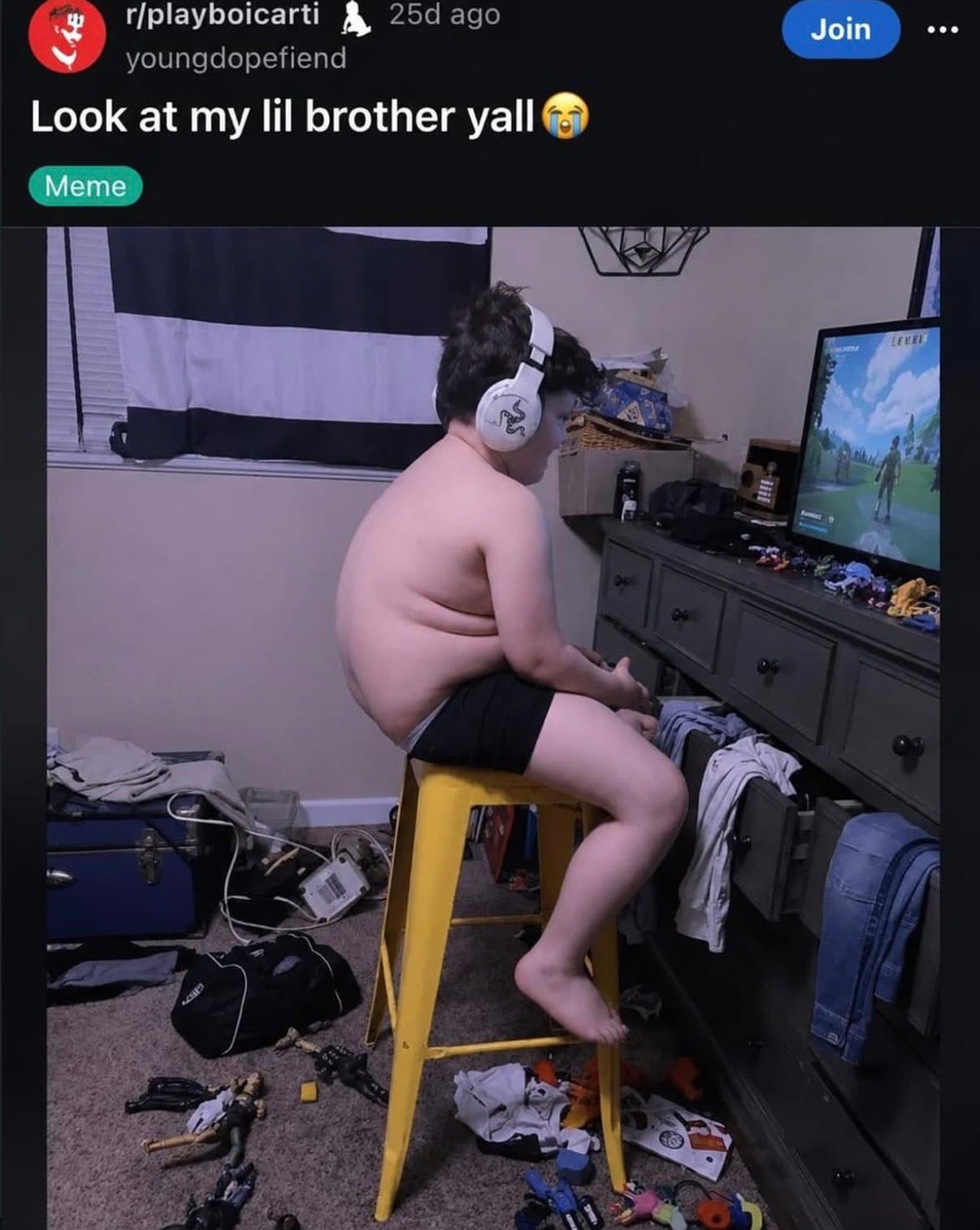 Reddit screenshot captioned 'Look at my lil brother yall' showing a shirtless kid hunched on a yellow stool wearing oversized headphones, playing a video game in a messy bedroom